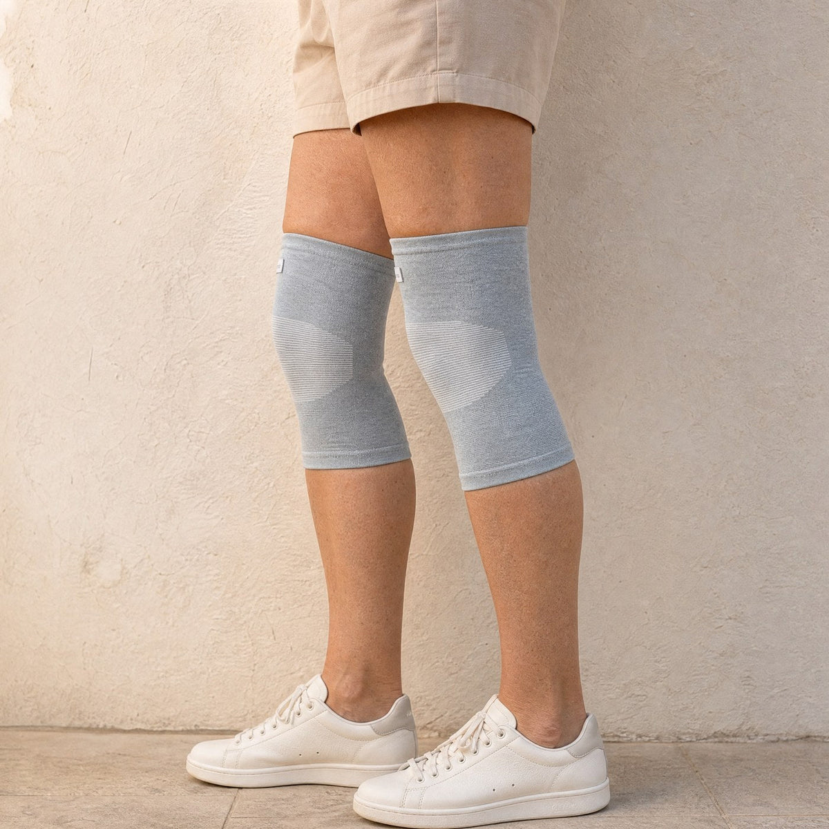 Genouillères de compression grises portées debout avec des baskets blanches